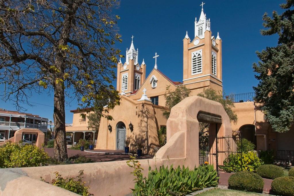 A vibrant scene of Albuquerque's Old Town Plaza with adobe buildings, artisan stalls, and the San Felipe de Neri Church